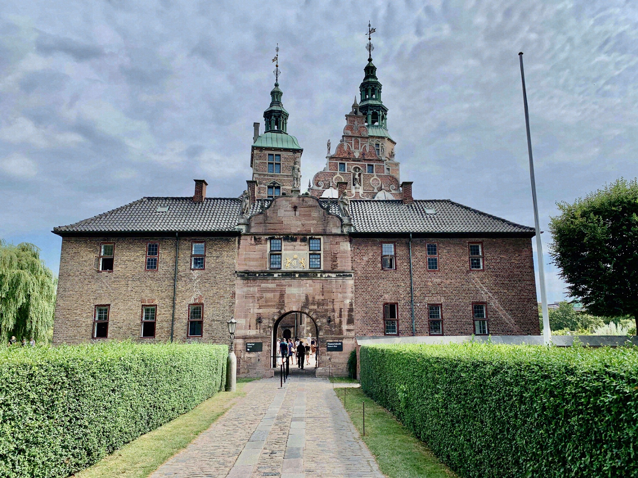 Frontansicht von Rosenborg Slot mit symmetrischem Toreingang, zwei gruenen Tuermschen und gepflegten Heckenrabatten im Vordergrund.